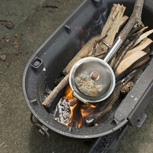Popcorn-eten-zintuigen-kamperen detailfoto van de popcornmaker liggend op het kampvuur